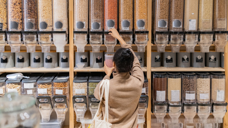 Woman fills container with dried food from bulk container at store