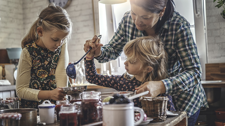 Woman helps children prepare home-canned jam in sunny farmhouse kitchen