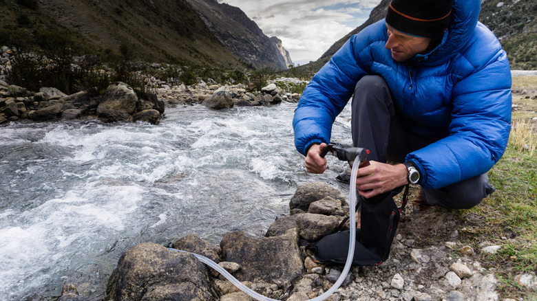 Man in blue jacket uses filter to collect water from rushing stream