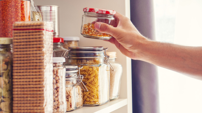 Man's hand moves small jar of corn from full pantry shelf