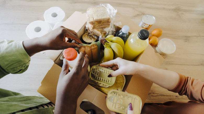 Hands pulling various foods from cardboard box on wood table