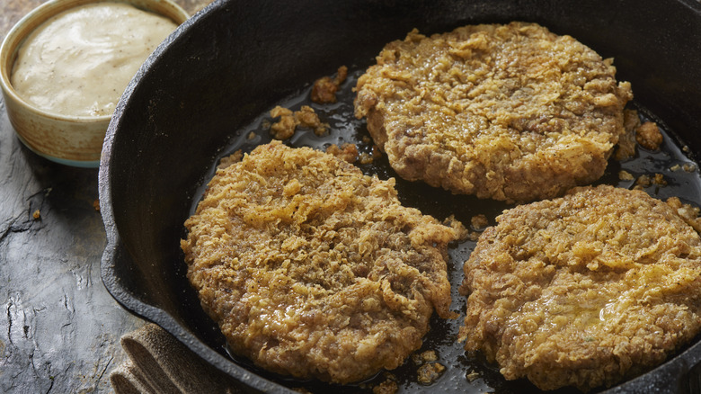 Three chicken fried steaks in large skillet with gravy pot on the side