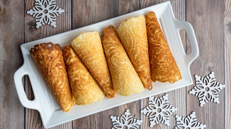 Krumkaker cookies from Norway rolled into cones and put on a white tray that is placed on wood surrounded with snowflake decorations