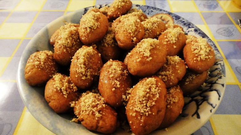 Melomakarona honey cookies sprinkled with nuts stacked in a bowl on a table