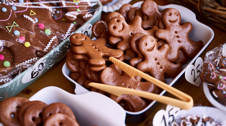 An assortment of decorated and plain gingerbread men stacked in trays on a wooden table