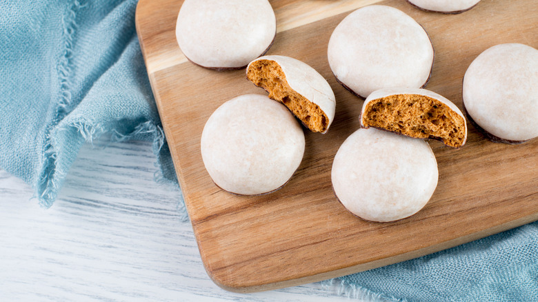 Whole and cut pfeffernüsse cookies on a wooden cutting board that is placed on a white table covered with blue linen