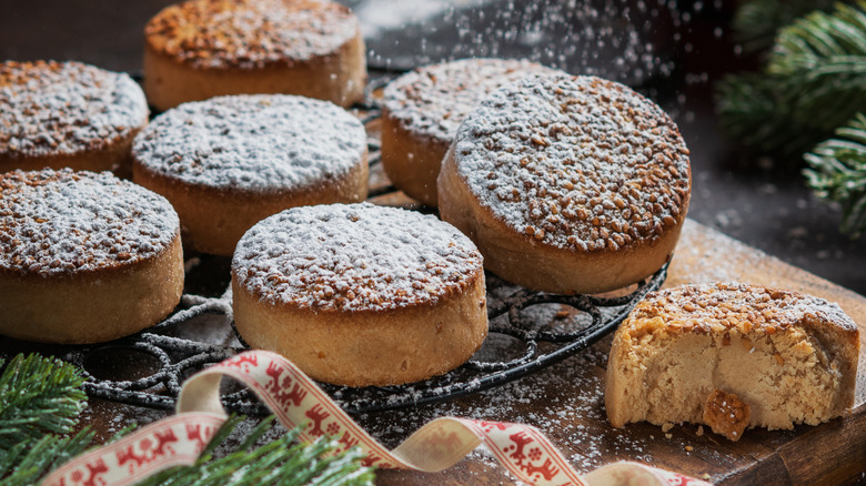 Spanish round polvorones cookies being dusted with sugar while they are set on a rack next to pine branches