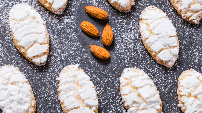 Ricciarelli cookies heavily decorated with sugar and four raw almonds assembled on a dark plate