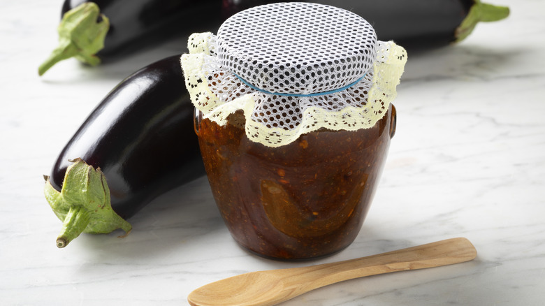 Eggplant chutney in glass jar with eggplants and spoon