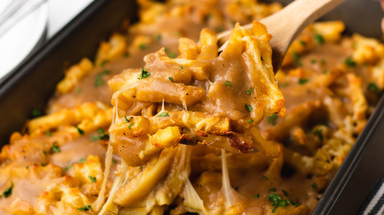 Scooping cheesy disco fries out of tray on wooden spoon