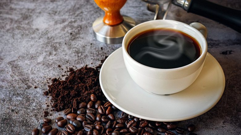 mug of black coffee with whole and ground beans