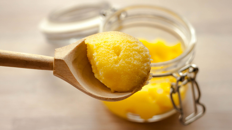 Ghee clarified butter desi yellow color in glass jar with spoon made from wood on natural wooden background close-up view