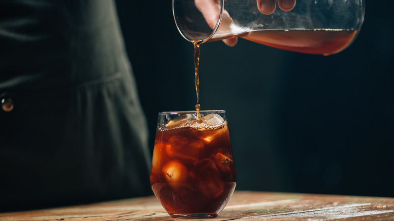 Hands of a barista pouring cold brew coffee over ice cubes