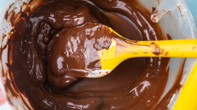 Bowl with melted chocolate and yellow spatula on blue background