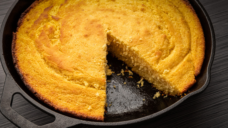 Cornbread inside of black cast iron skillet with triangular slice missing