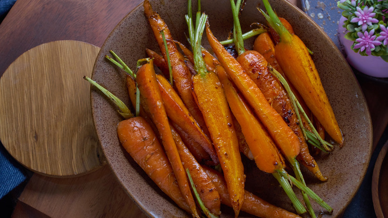 A brown ceramic bowl with roasted whole and halved baby carrots