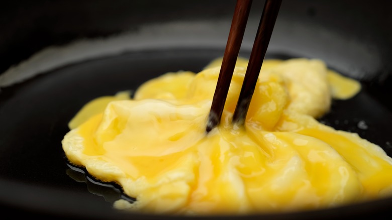 Chopsticks stirring eggs in pan