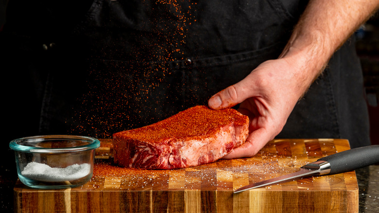 Chef seasoning a raw New York strip steak