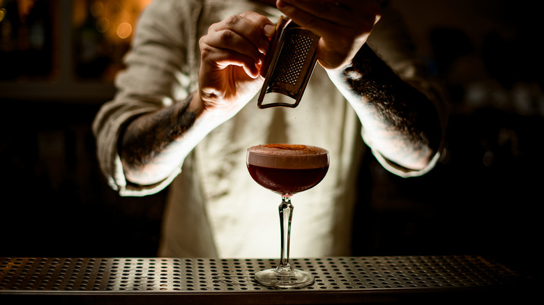 bartender grates cinnamon atop cocktail