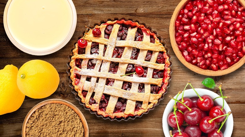 Cherry pie surrounded by ingredients on wooden table