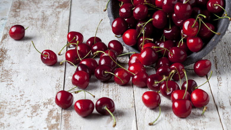 Fresh cherries spilling out of a bowl onto a wooden table