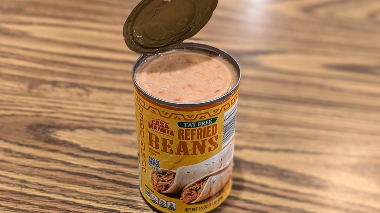 Open can of Casa Mamita fat-free refried beans on wood table