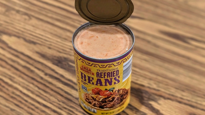 Open can of Casa Mamita traditional refried beans on wood table