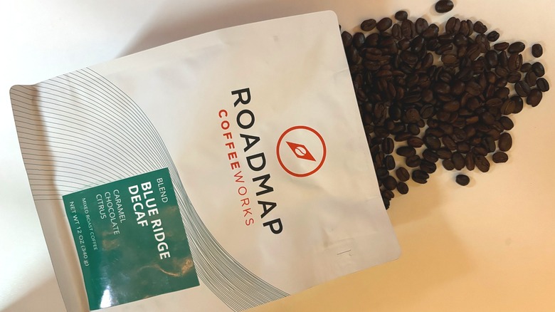 Coffee beans spilling out of a bag of Roadmap decaf coffee onto a white table