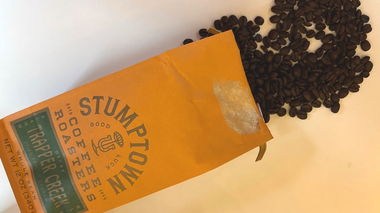 Coffee beans spilling out of an orange Stumptown decaf bag onto a white table