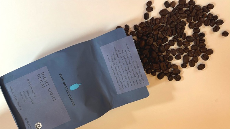 Coffee beans spilling out of a blue bag of Blue Bottle coffee onto a white table