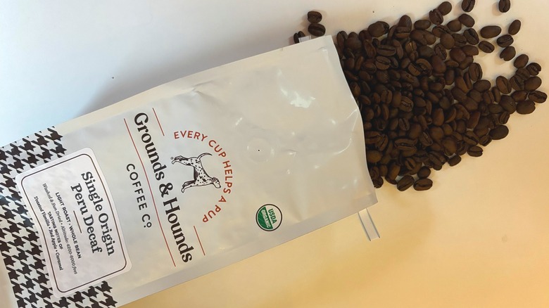 Coffee beans spilling out of a Grounds & Hounds Peru Decaf bag onto a white table