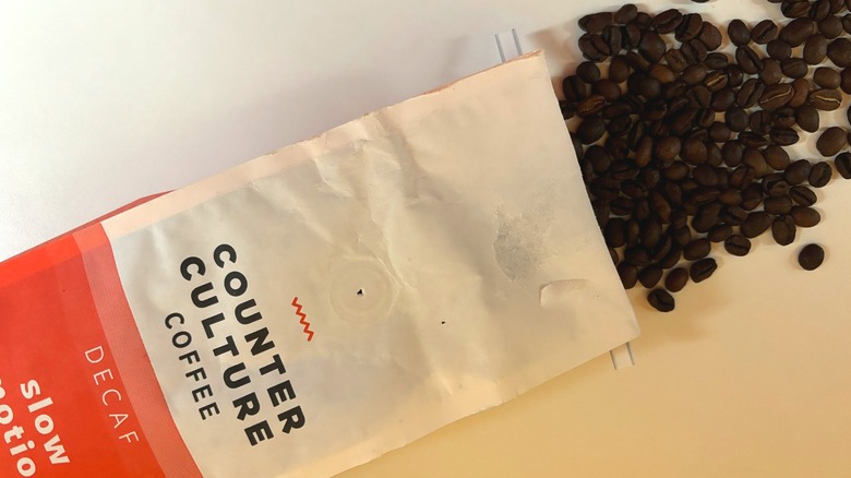 Coffee beans spilling out of a Counter Culture Slow Motion decaf coffee bag onto a white table