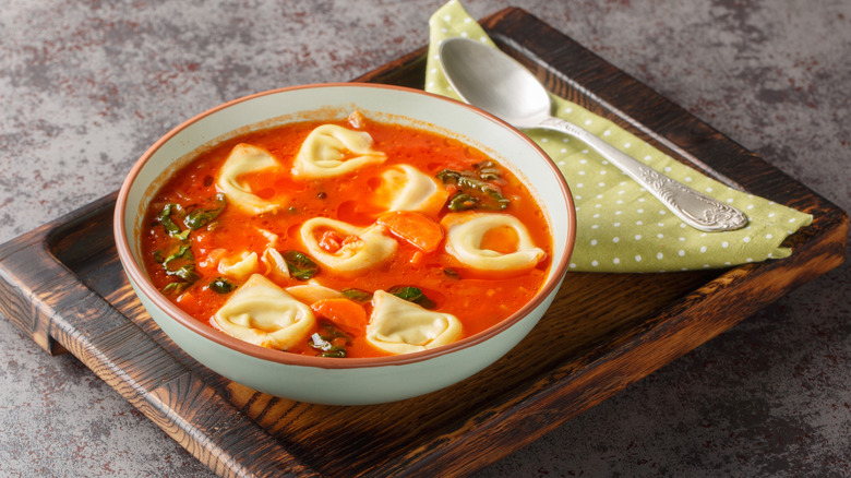 Bowl of tomato tortellini soup on a wooden serving tray