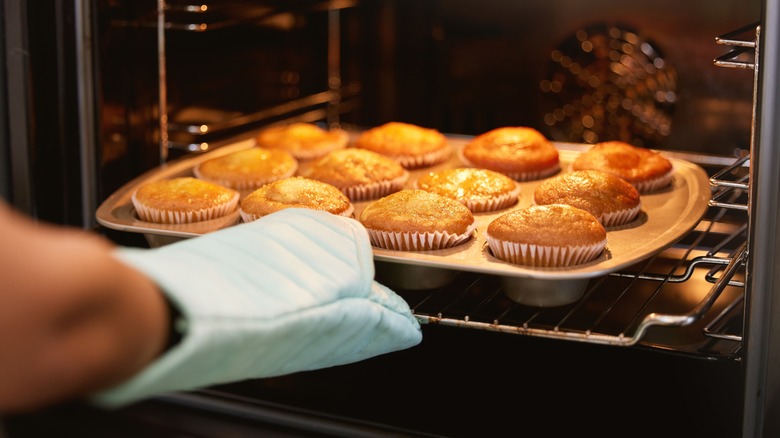 Person baking muffins in oven