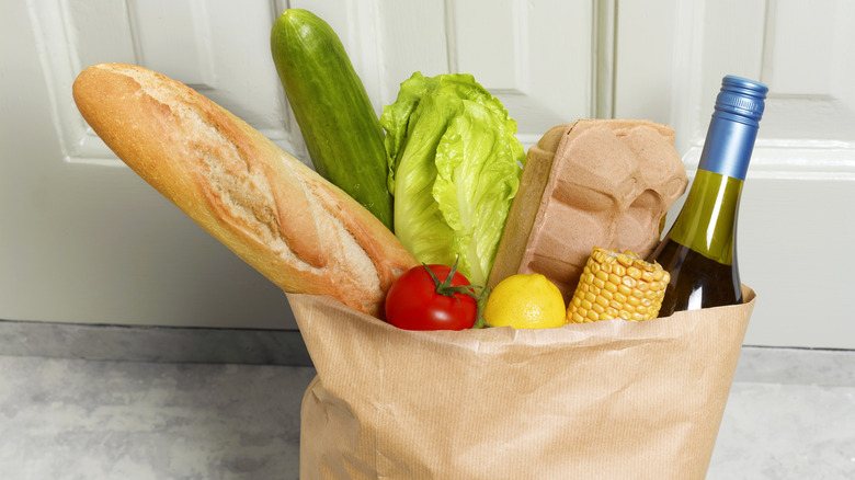 grocery bag with loaf of bred, vegetables, egg carton, and wine bottle inside