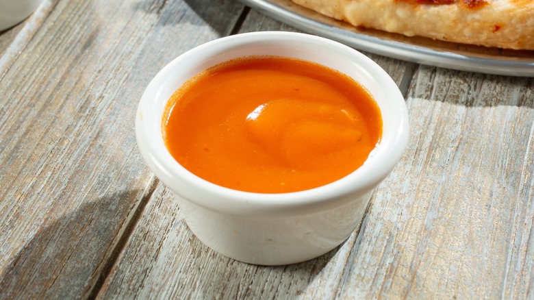 A ramekin of buffalo sauce on a wood table