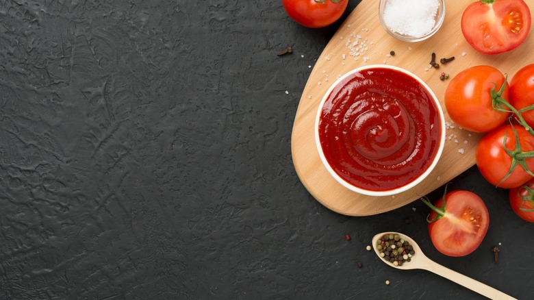 A dish with ketchup next to tomatoes and spices