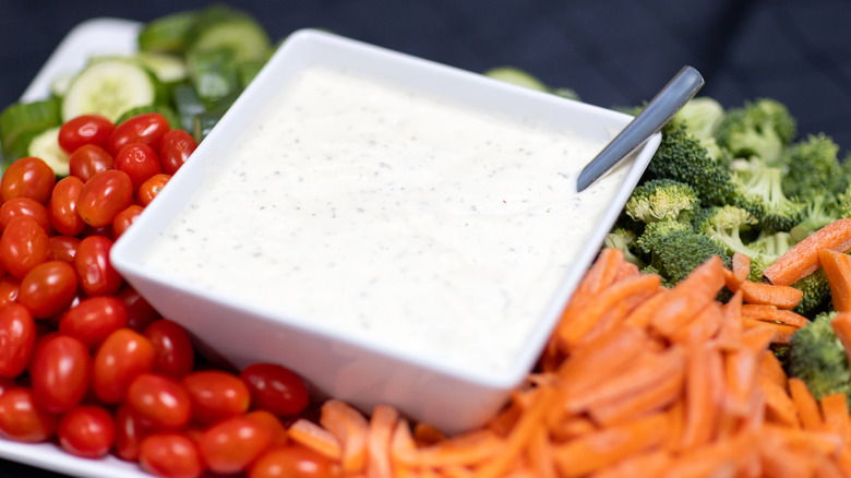 A bowl of ranch next to fresh vegetables