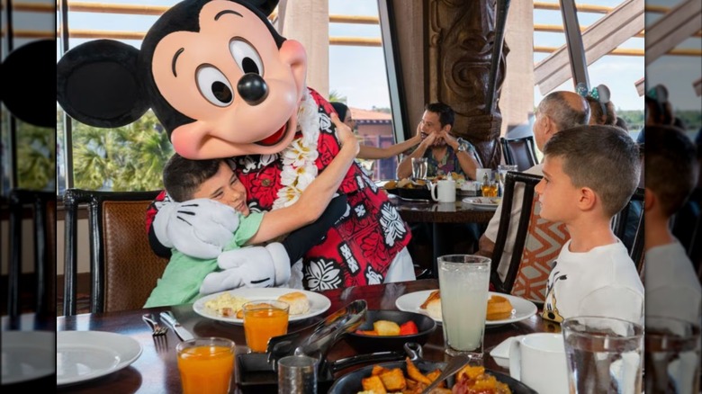 Child hugging Mickey Mouse while enjoying a meal at Ohana restaurant in Disney World
