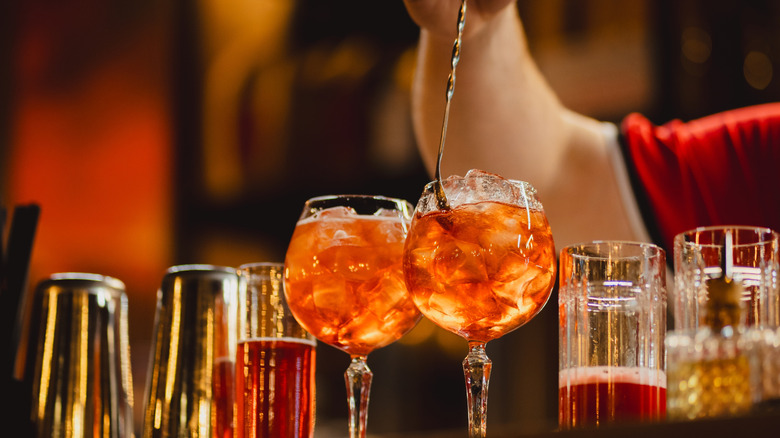 Bartender stirring orange cocktail goblets with bar spoon