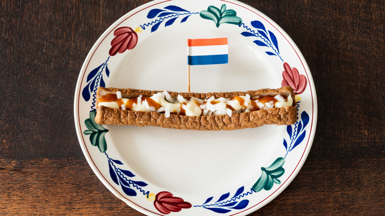 Frikandel sausage topped with onions and sauce on a decorative plate