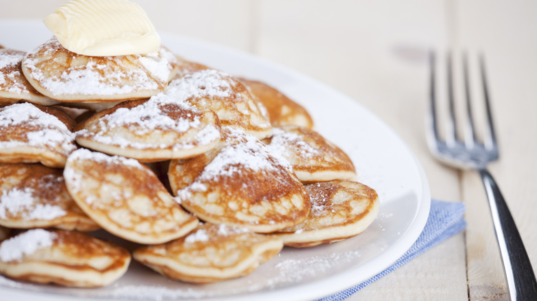 Pile of poffertjes, small Dutch pancakes, with butter and icing sugar on a plate