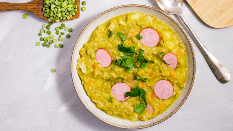 Bowl of Dutch pea soup garnished with sliced sausage and herbs