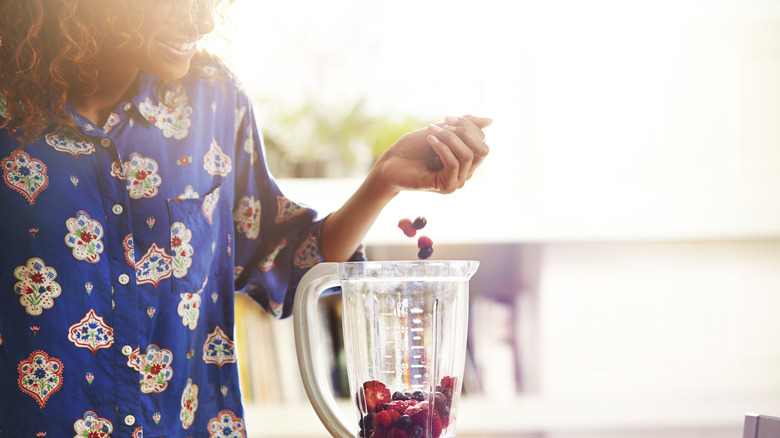 A woman adding berries to a blender