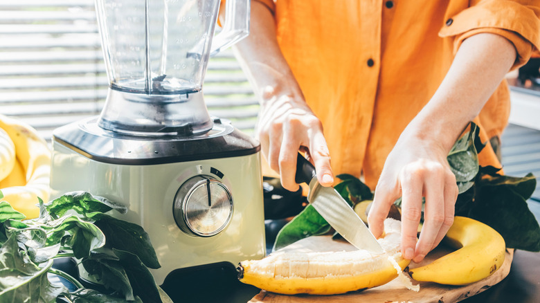 A person cutting a banana to make a smoothie