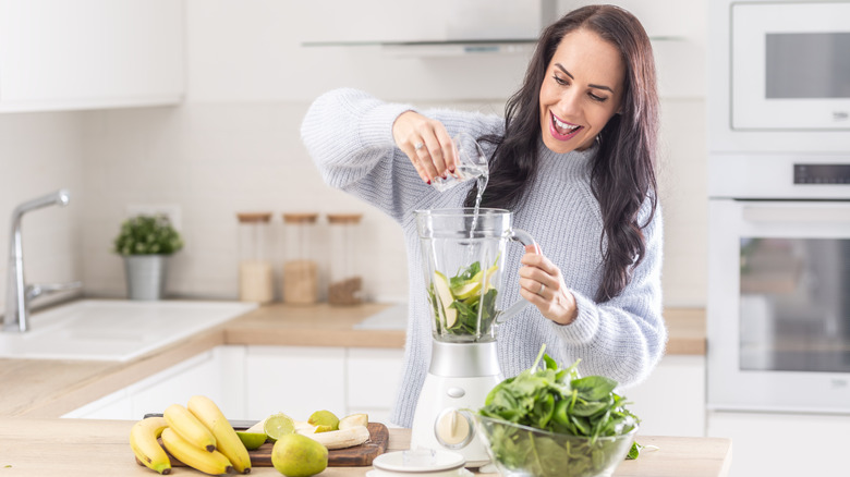 A woman pouring water into a blender