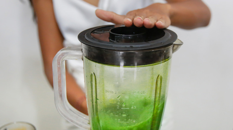 A person with their hand on a blender's lid