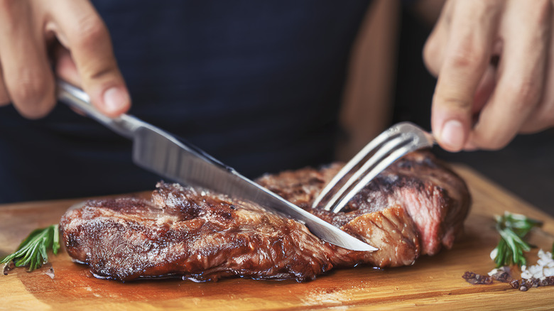 A person cutting a piece of steak on a wooden board