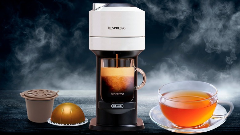 Nespresso machine brewing coffee, reusable coffee pod, Nespresso pod, and cup of tea against smoky black background