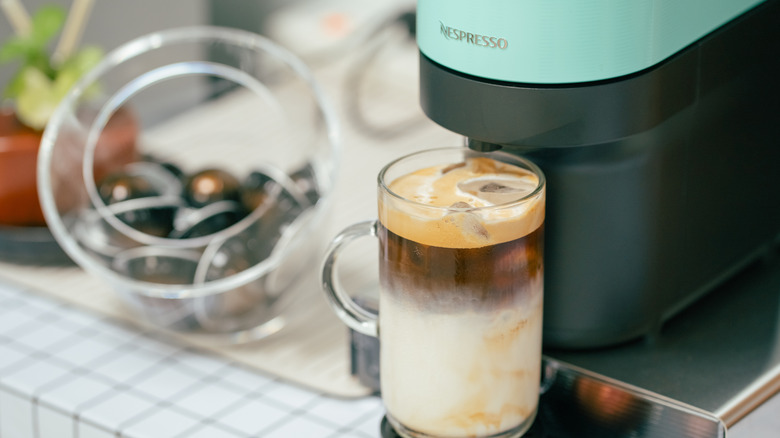 Teal colored Nespresso machine with freshly brewed iced latte